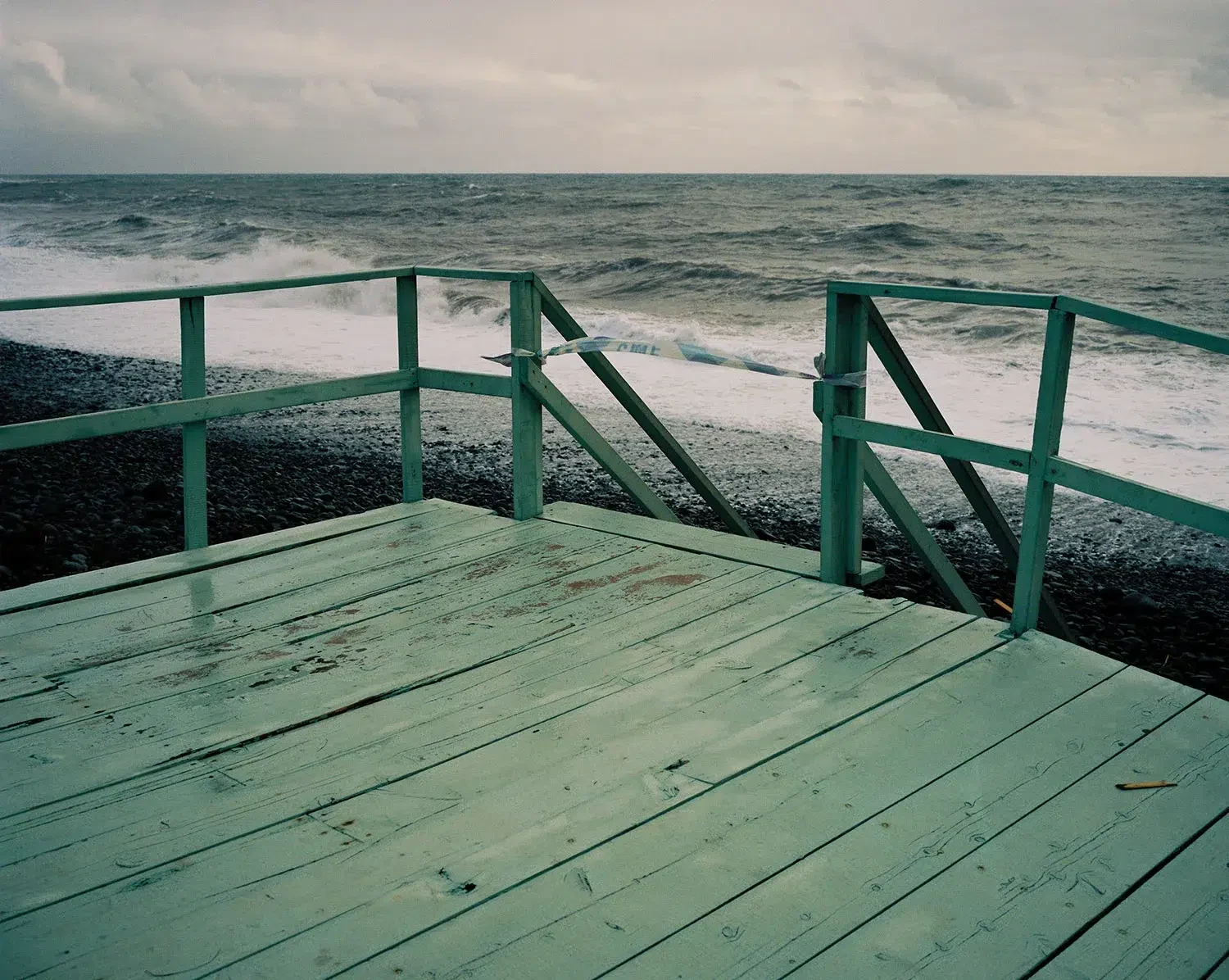 A green wooden platform and railings face a rough sea beneath an overcast sky.