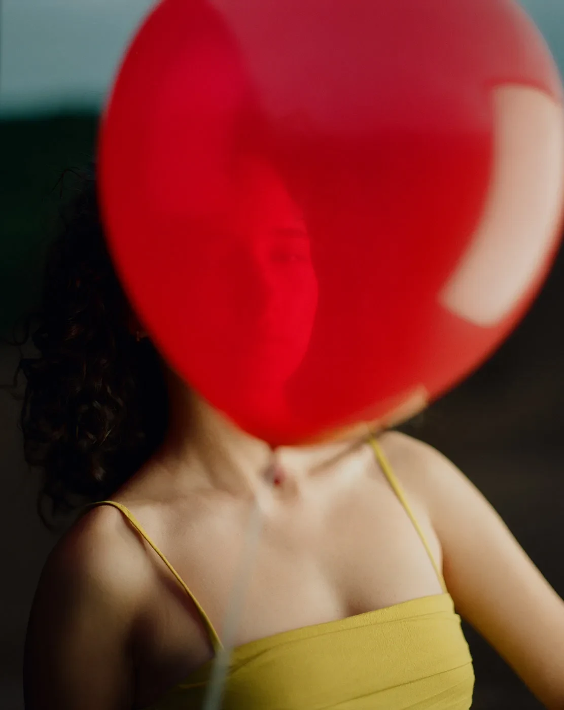 A red balloon obscures the face of a person wearing a yellow top.
